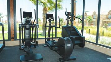 A gym with cardio machines and a view of a landscaped area with palm trees.