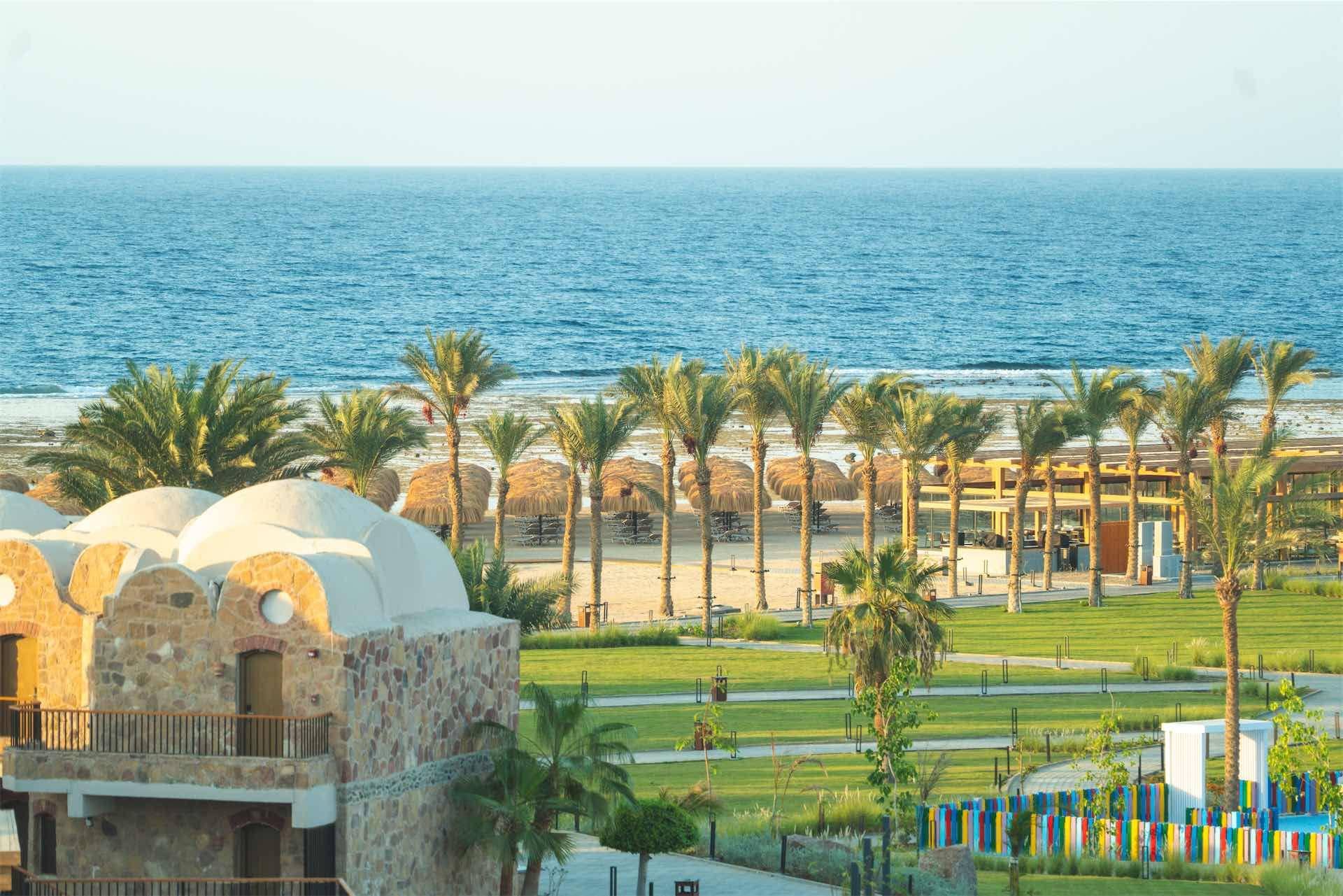 Un hotel frente al mar con arquitectura de piedra, palmeras y vistas al océano.