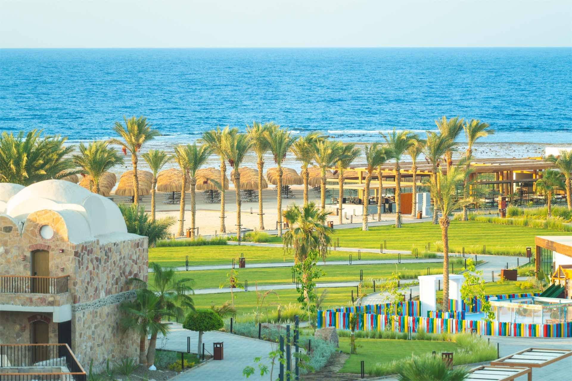 A resort with a view of the sea, palm trees, and a building with a dome.
