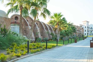 A paved pathway lined with palm trees and a stone building with arched windows. - Acel Beach Resort Hotel (El Quseir)