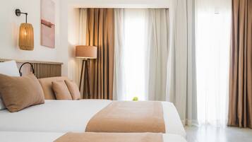 Une chambre d’hôtel avec deux lits, une lampe sur pied, une applique murale et une grande fenêtre avec des rideaux.