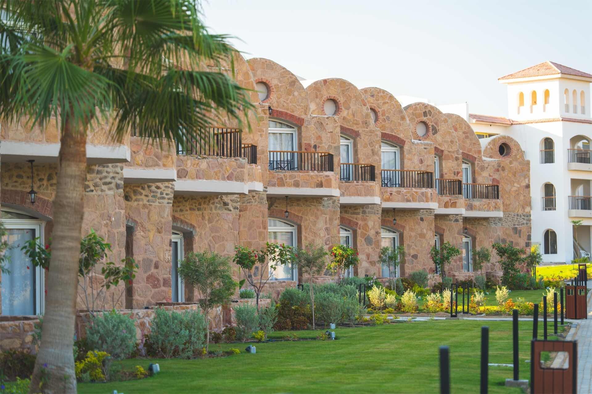 Um hotel com fachada de pedra, varandas e um jardim bem cuidado, sob um céu limpo.