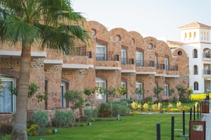 Un hotel con balcones de fachada de piedra, un jardín bien cuidado y cielo despejado.
