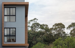 A modern building with two visible windows and a view of dense trees in the background. - Duna Loft overlooking the Lagoon | Pool and gym (Florianópolis)