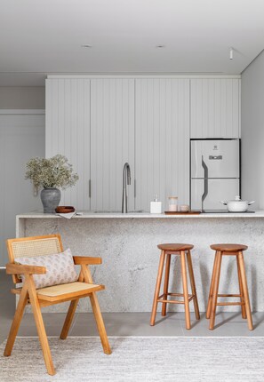 A modern kitchen with a marble countertop, a built-in sink, a stainless steel faucet, a white refrigerator, and wooden stools. - Duna Loft overlooking the Lagoon | Pool and gym (Florianópolis)