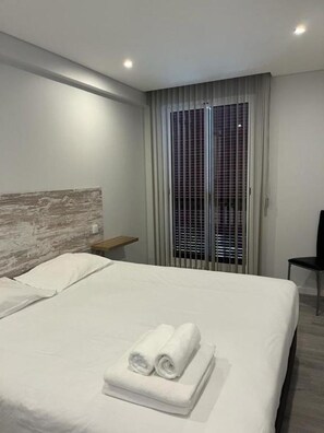A hotel room with a bed, a nightstand, a chair, and a window with blinds. - Ocean Paradise—is it? (Funchal)