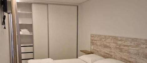 A modern bedroom with a large bed, a wardrobe, and a bedside table.