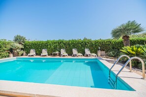 Ein Schwimmbad mit Liegestühlen und einer Hecke im Hintergrund.