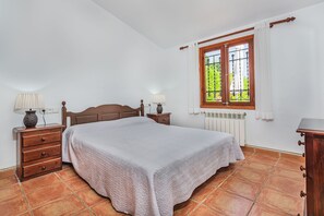Een slaapkamer met een houten bed, twee nachtkastjes met lampen, een raam met gordijnen en een radiator.