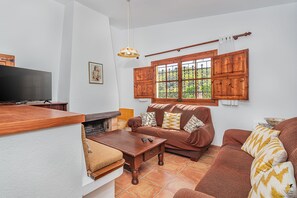 Ein Wohnzimmer mit Fernseher, Holzmöbeln, Kamin und einem Fenster mit Holzläden.