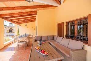 Um pátio externo com mesa de madeira, cadeiras, um sofá e uma cesta de frutas.