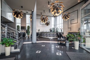 Ett modernt receptionsområde med en böjd receptionsdisk, svarta lädersitsar och en trappa med metallräcken.
