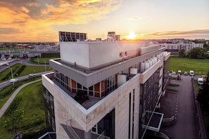 Een modern gebouw met een plat dak en grote ramen, omgeven door een groen landschap en een weg.