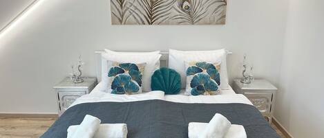 A neatly made bed with a dark quilt, two pillows with a leaf pattern, and a wall-mounted artwork above.