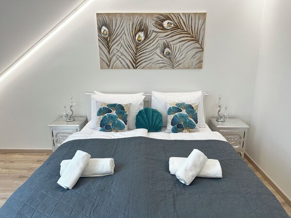 A neatly made bed with a dark quilt, two pillows with a leaf pattern, and a wall-mounted artwork above.