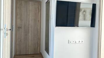 A hallway with a wooden door, a mounted TV, and a power outlet on the wall.