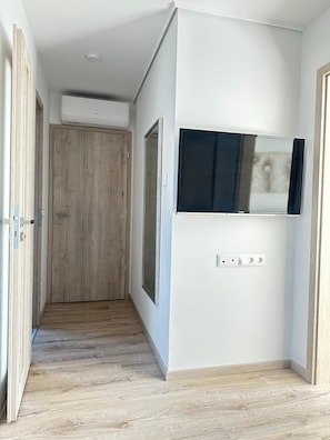 A hallway with a wooden door, a mounted TV, and a power outlet on the wall. - Exclusive 1 bedroom suite at Vác Danube Bend (Budapest)