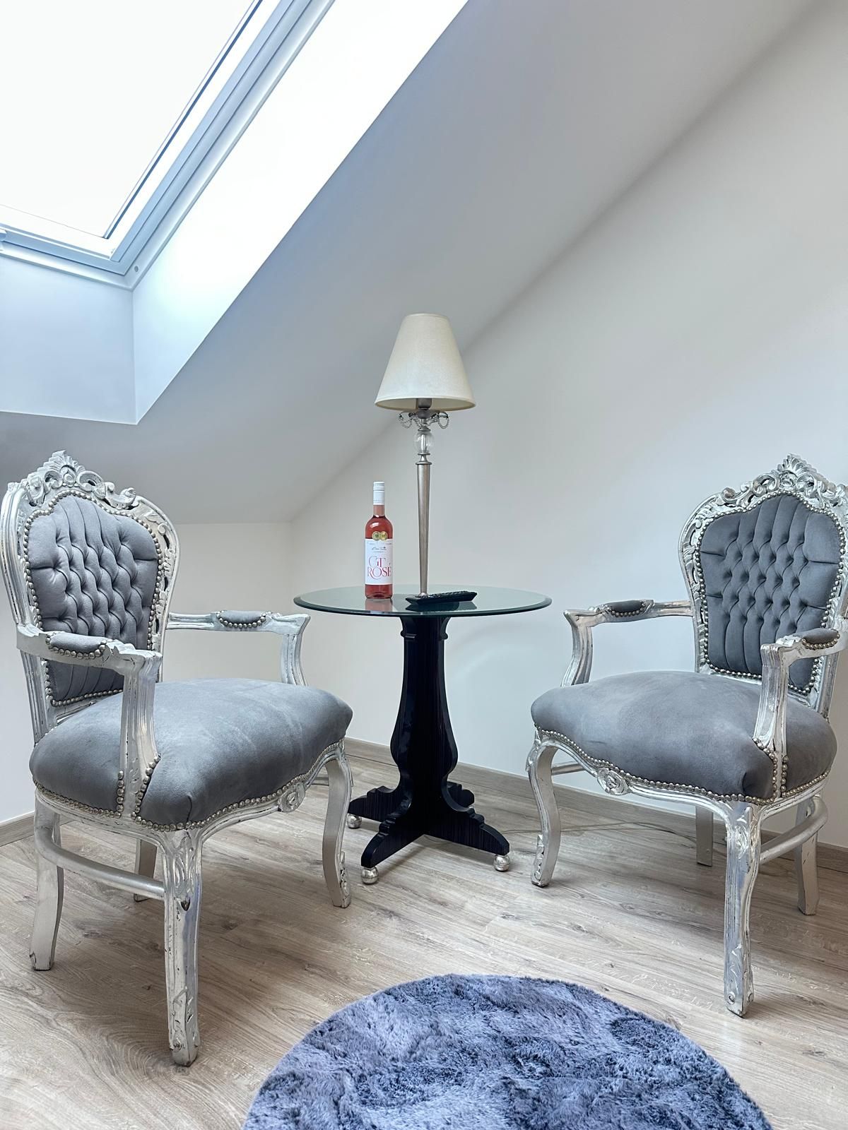 A room with two ornate chairs, a small round table, a floor lamp, and a blue rug.