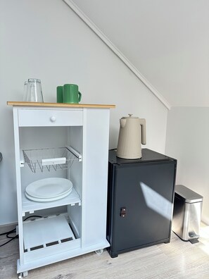 A white storage unit with a wooden top shelf, a metal rack, and a black cabinet with a kettle on top. - Exclusive 1 bedroom suite at Vác Danube Bend (Budapest)