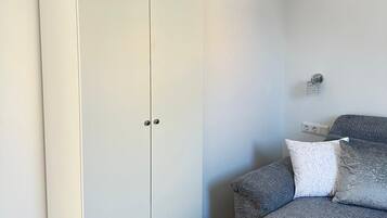 A bedroom with a grey sofa, a white wardrobe, and a wall-mounted light fixture.