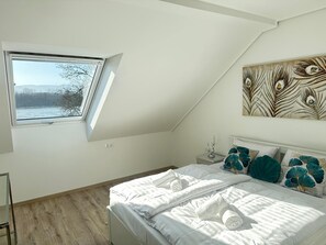 Ein Schlafzimmer mit Dachfenster, einem Bett mit weißen Leinentüchern, türkisfarbenen Kissen und einem an der Wand hängenden Kunstwerk.