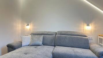 A modern living room with a sectional sofa, two wall-mounted lights, and a ceiling light.