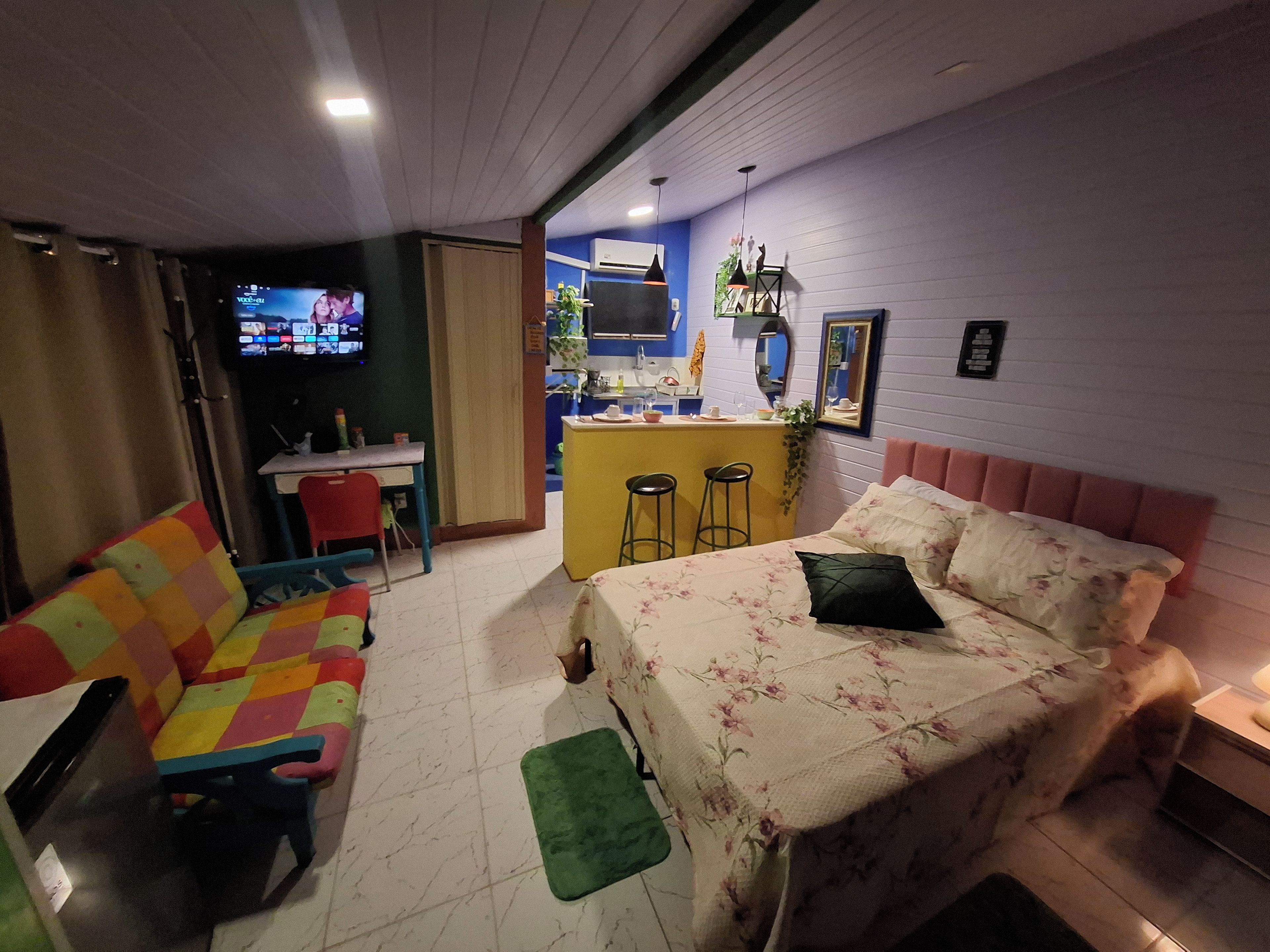 Ein Zimmer mit einem Bett, einem farbenfrohen Sofa, einem kleinen Tisch und einer Küchenzeile.