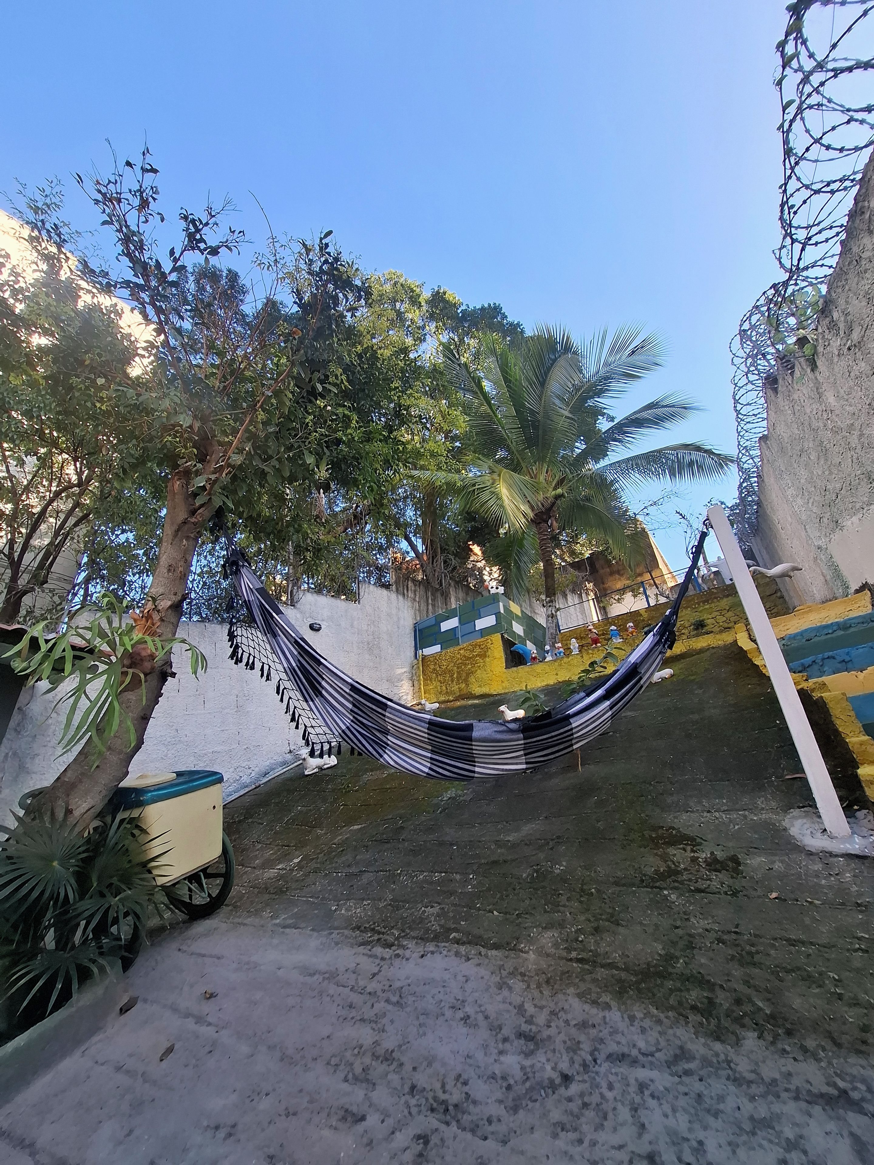 A hammock between trees in a courtyard with a white wall and a colorful mural.