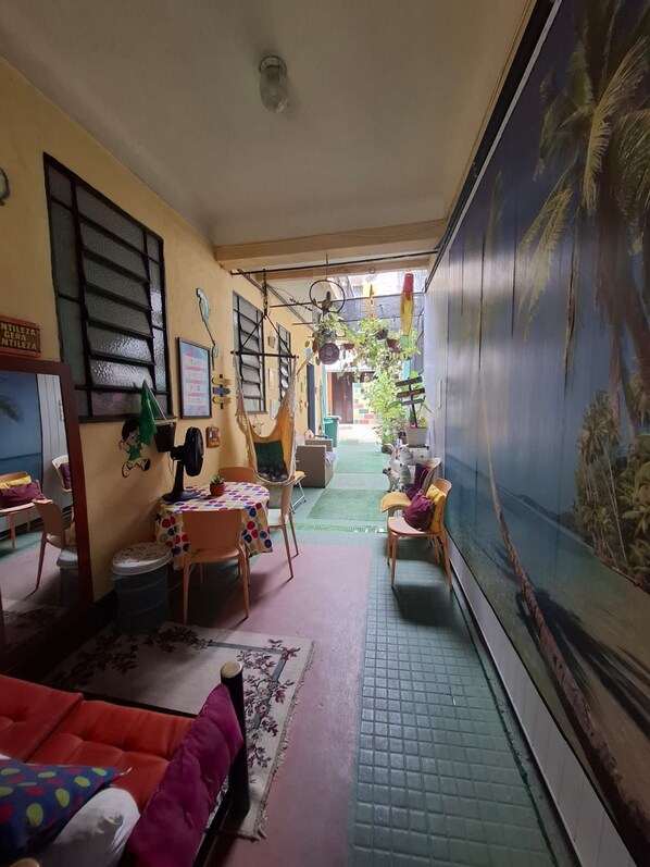 A cozy living room with a sofa, a table, and a TV screen. There is a window with blinds and a door leading to another room.