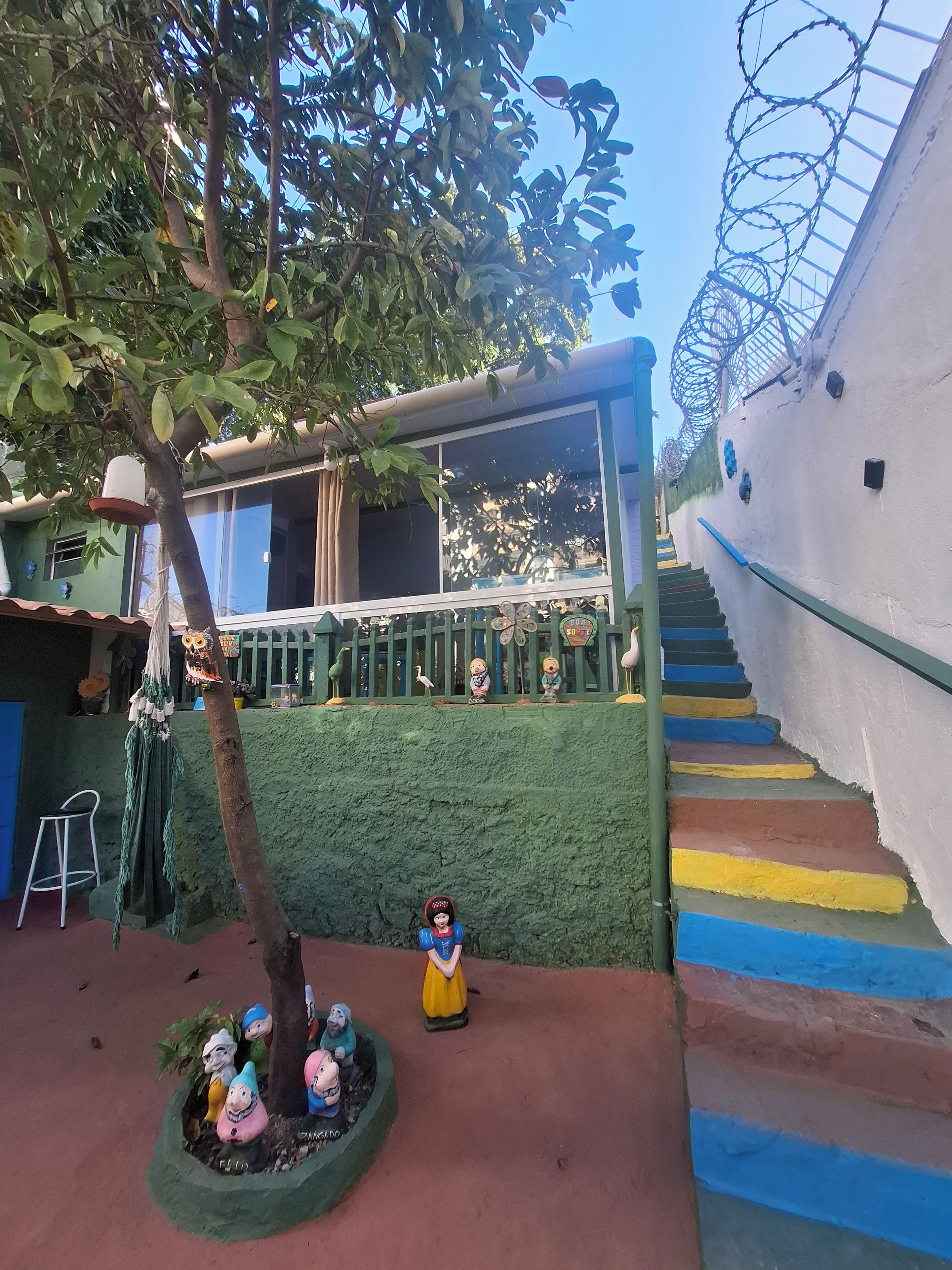 A staircase with colorful steps leading up to a green-roofed structure, surrounded by decorative statues and a tree.