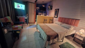A hotel room with a bed, bedside tables, a desk with a chair, a television, and a small bar area.