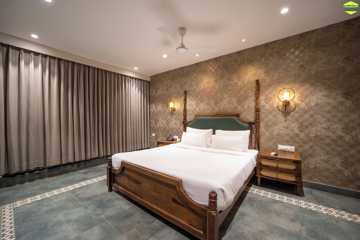A hotel room with a large bed, a ceiling fan, a nightstand, and a wall-mounted lamp.