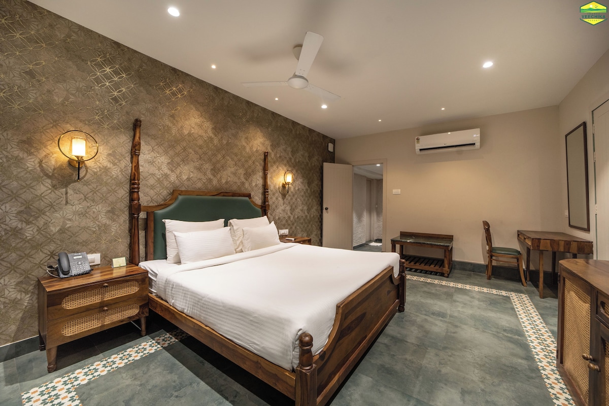 A hotel room with a large bed, bedside lamps, a desk, a chair, and an air conditioning unit.