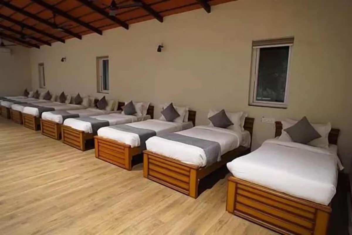 A row of wooden beds with white linens and gray pillows in a room with a wooden floor and a sloped ceiling.
