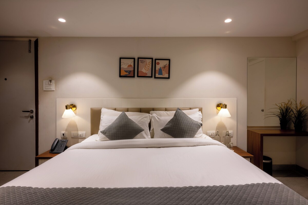 A hotel room with a large bed, two bedside lamps, a nightstand with a phone, and a mirror on the wall.