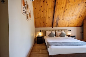 A bedroom with a wooden ceiling, a bed with multiple pillows, bedside tables with lamps, and a wall-mounted phone.