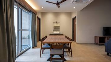 A spacious room with a large dining table, chairs, a ceiling fan, a TV, and a large window with curtains.