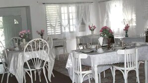 A dining area with white tables and chairs, covered with white tablecloths, and adorned with pink flowers. - Serenity Cove Resorts (St. Ann Parish)