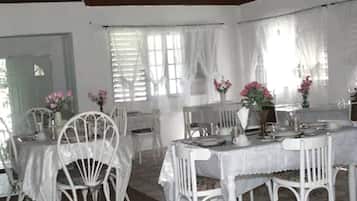 A dining area with white tables and chairs, covered with white tablecloths, and adorned with pink flowers.