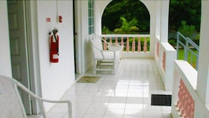 A covered outdoor area with white chairs, a fire extinguisher, and a view of greenery. - Serenity Cove Resorts (St. Ann Parish)