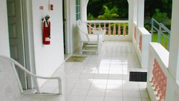 A covered outdoor area with white chairs, a fire extinguisher, and a view of greenery.