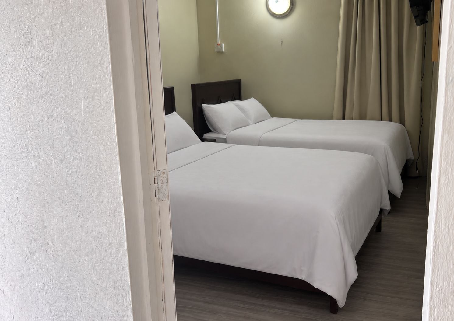 Een hotelkamer met twee eenpersoonsbedden, een nachtkastje, een wandlamp en een gordijn.