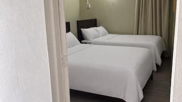 Habitación de hotel con dos camas individuales, una mesita de noche, una lámpara de pared y una cortina.