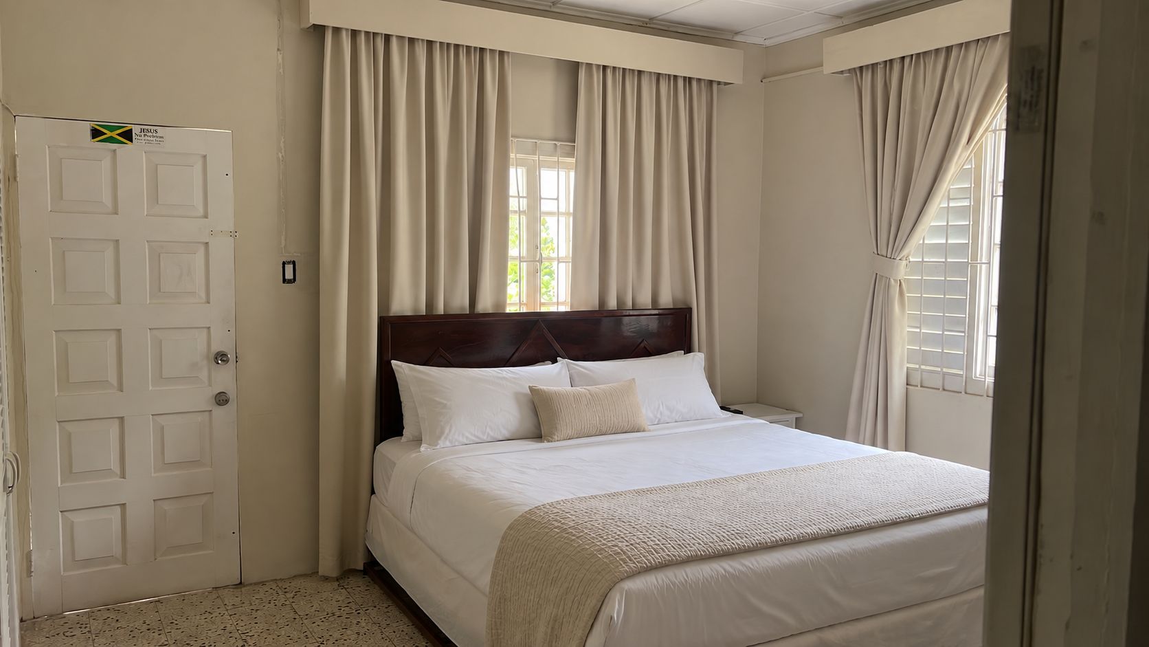 A bedroom with a bed, curtains, a door, and a window.