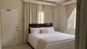A bedroom with a bed, curtains, a door, and a window. - Serenity Cove Resorts (St. Ann Parish)