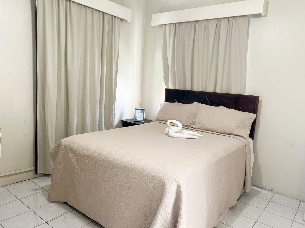 Quarto de hotel com cama, cortinas, mesa de cabeceira e almofada em formato de cisne.