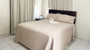 A hotel room with a bed, curtains, a nightstand, and a swan-shaped pillow. - Serenity Cove Resorts (St. Ann Parish)
