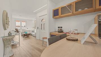 Une cuisine moderne avec un plan de travail en bois, un coin repas doté d’une table en verre et un salon avec un canapé et un élément décoratif mural.