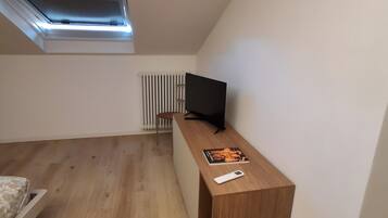 Una stanza con soffitto spiovente, una scrivania in legno con televisione, un termosifone e un letto.