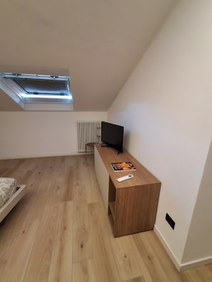 Ein Zimmer mit schrägem Dach, einem Holztisch mit Fernseher, einem Heizkörper und einem Bett.